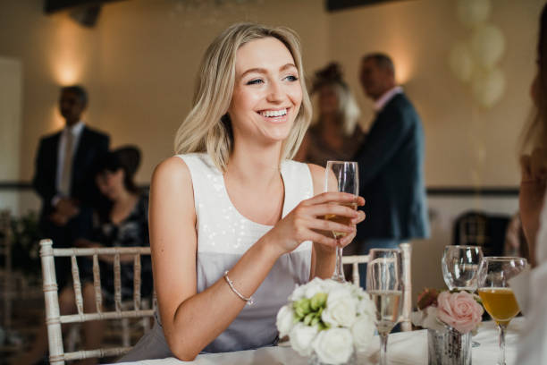 young woman is sitting at a table at a wedding with a glass of champagne.